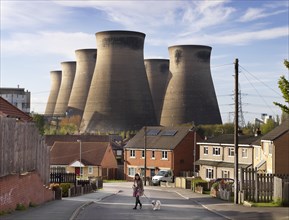 Ferrybridge C Power Station, West Yorkshire, 2018. General view looking north-west along a suburban street, with a woman walking a dog in the foreground and the power station's cooling towers dominati...