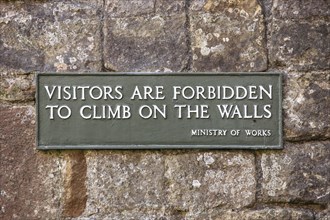 Notice on the wall of Lanercost Priory, Cumbria, 2018. Detail of a Ministry of Works sign reading 'Visitors are forbidden to climb on the walls' on the side of the priory.