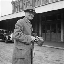 John Laing holding a Rolleiflex camera outside Bournemouth train station, 30/05/1953. Creator: John Laing plc.