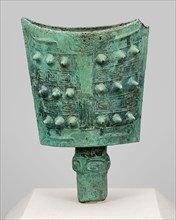 Bell (nao), Western Zhou dynasty (1046-771 B.C.). A bell with two convex sides of nearly rectangular shape and an opening at top rests on a slim cylindrical base. It boasts a green patina and is decor...