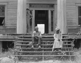 Ex-slave and wife on steps of plantation house now in decay, Greene County, Georgia, 1937. Creator: Dorothea Lange.