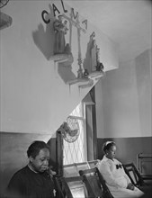 Sitting beneath the emblem of the crucifixion of Jesus on Calvary, Washington, D.C., 1942. Creator: Gordon Parks.