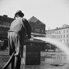 Workmen from the sanitary department flushing the street in front of the Fulton..., New York, 1943. Creator: Gordon Parks.