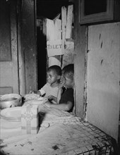 Three children waiting in the kitchen while their mother prepares the..., Washington, D.C, 1942. Creator: Gordon Parks.
