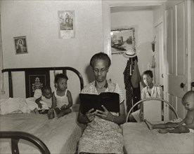Washington, D.C. Mrs. Ella Watson, a government charwoman, reading the Bible to her household.