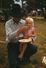 Homesteader feeding his daughter at the Pie Town, New Mexico Fair free barbeque, 1940. Creator: Russell Lee.