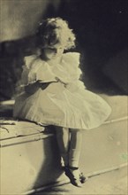 Seated girl reading a book, c1900.