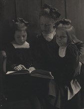 Three young girls reading a book, c1900.