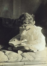 Girl sitting with legs folded, reading a book, c1900.