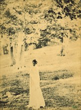 Woman standing in a park, trees in background, c1900.