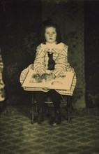 Girl in a plaid dress seated with a book in her lap, c1900.