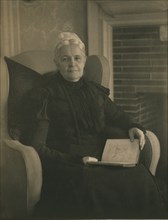 Old woman in an armchair, with an open book in her lap, c1900.