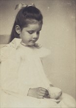 Young girl in white dress, seated holding teacup and saucer, c1900.