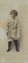 Portrait of a young boy standing in short pants and belted shirt, c1900.