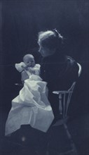 Woman, sitting in chair, holding an infant, full-length portrait, c1900.