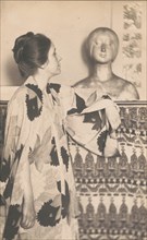 Woman wearing a kimono, standing, looking at a sculpted bust, c1900.