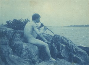 Man posed on rocks, nude, playing pipe (Pan), between 1885 and 1900.