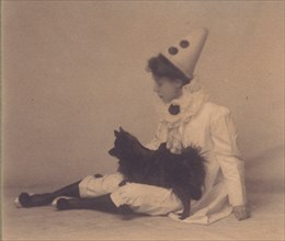 Girl dressed in a pierrot costume with a small black dog on her lap, between 1900 and 1920.