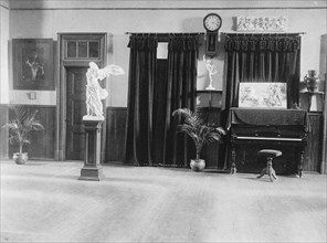 Room with piano, potted palms, and classical statues and friezes, (1899?).