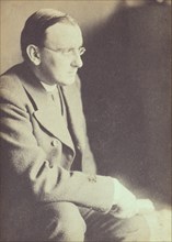 Portrait of man wearing glasses, seated with elbow resting on right knee , c1900.