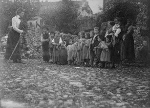 Frances Benjamin Johnston photographing a group of people, mostly children, in Europe, 1900.