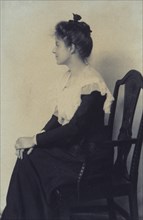 Profile portrait of a woman seated in chair, facing left with hands on her knees, c1900.