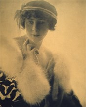 Half-length portrait of a woman wearing a fur trimmed coat, facing front, between 1900 and 1920.