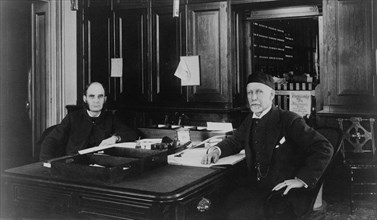 Two Treasury Department employees seated at desk in office, between 1884 and 1930.