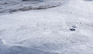 Walkers on a snowy Ingleborough Hillfort, with hut circle earthworks also visible, North Yorkshire, 2018.
