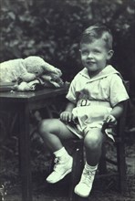 Portrait of a young boy seated at an outdoor table, facing front, between 1940 and 1950.