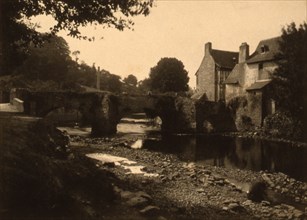 View of a stone bridge, river and buildings in a village, probably in France , c1890.