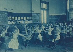 Children doing calisthenics while sitting at their desks in a classroom, 5th Division public schools, Washington, D.C., (1899?).