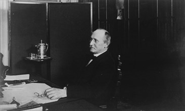 Gen. Shelley, Treasury Department employee, half-length portrait, seated at desk, facing left, between 1884 and 1930.