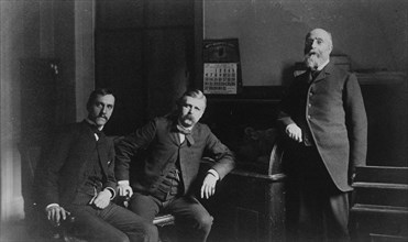 Three Treasury Department employees, Mr. Steele(?) and two other men, posed in office, between 1884 and 1930.