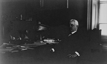 Gov. Thompson(?), Treasury Department employee, half-length portrait, seated at desk, facing left, between 1884 and 1930.