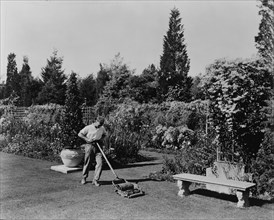 Gardener pushing lawn mower, posed to illustrate Rudyard Kipling's poem "The Glory of the Garden", 1917.