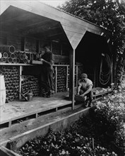 Gardeners potting plants in a shed, posed to illustrate Rudyard Kipling's poem "The Glory of the Garden", 1917.