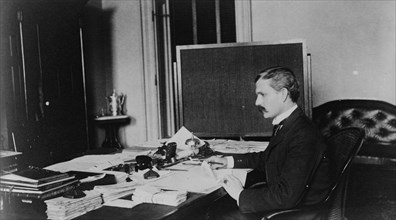 Dr. Miller, Treasury Department employee, half-length portrait, seated at desk, facing left, between 1884 and 1930.
