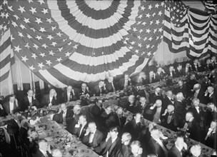 Banquet Scene with Flag Draping And Men Seated Holding Up Listening Device To One Ear, between 1913 and 1917.