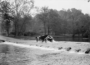 Couple In Automobile Fording A River At A Low Water Crossing Near A Small Stone Bridge, between 1913 and 1918.