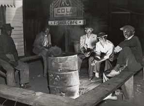 Negro laborers sitting around in front of a fire on Saturday night in a street of the..., Feb 1941. Creators: Farm Security Administration, Marion Post Wolcott.