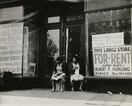 Sidewalk sitters. Two women sitting in doorway of empty storefront that is being..., ca. 1930s. Creator: Unknown.