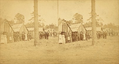 Group lined up in front of a row of shacks, (1868-1900?). Creator: Unknown.
