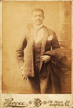 Dapper man, coat draped over his arm, and cane in hand, c1880-c1889. Creator: Unknown.
