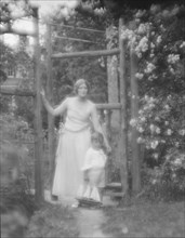 Conroy, Frank, Mrs., and child, standing by a garden gate, 1923 Creator: Arnold Genthe.