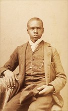 Studio portrait of unidentified seated young man, holding cap, c1880-c1889 . Creator: A. H. Plecker.