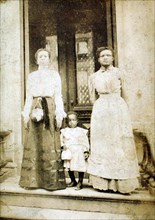 Two women and a child standing on step in front of a doorway of a house, c1900. Creator: Eckehard Munck.