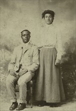 Studio portrait of a young couple, he seated, she with hand on his shoulder, c1900. Creator: Carbon Studio.