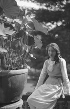 Unidentified woman seated in a garden next to a large potted plant, between 1917 and 1934. Creator: Arnold Genthe.