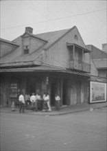 View from across street of a group of men on a street corner, New Orleans, between 1920 and 1926. Creator: Arnold Genthe.